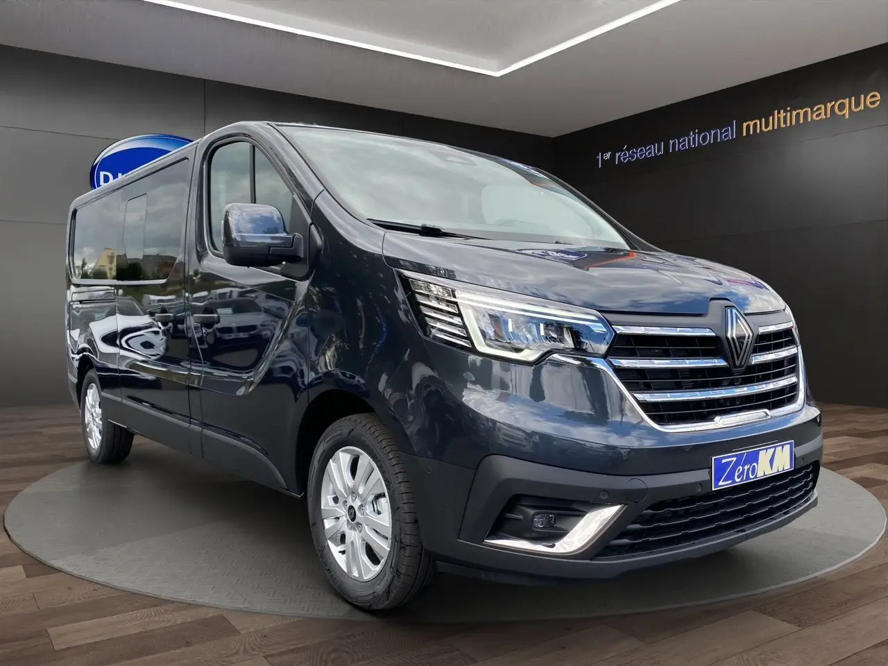 Renault Trafic cabine approfondie gris comète vu en 3/4 avant droit avec calandre chromée et phares LED allumés.