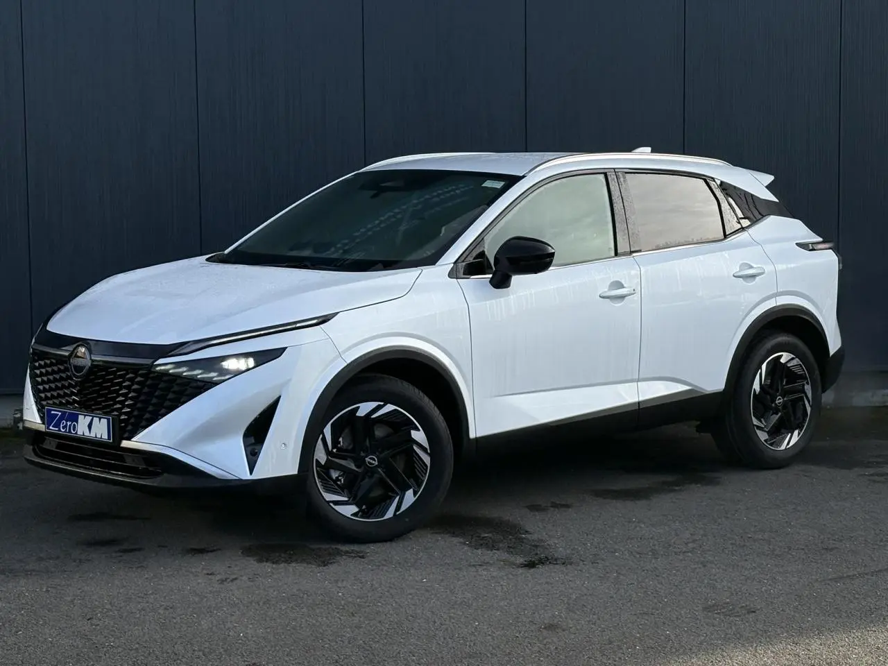 Nissan Qashqai blanc nacré en 3/4 avant droit, avec jantes alliage noires et toit contrasté noir.