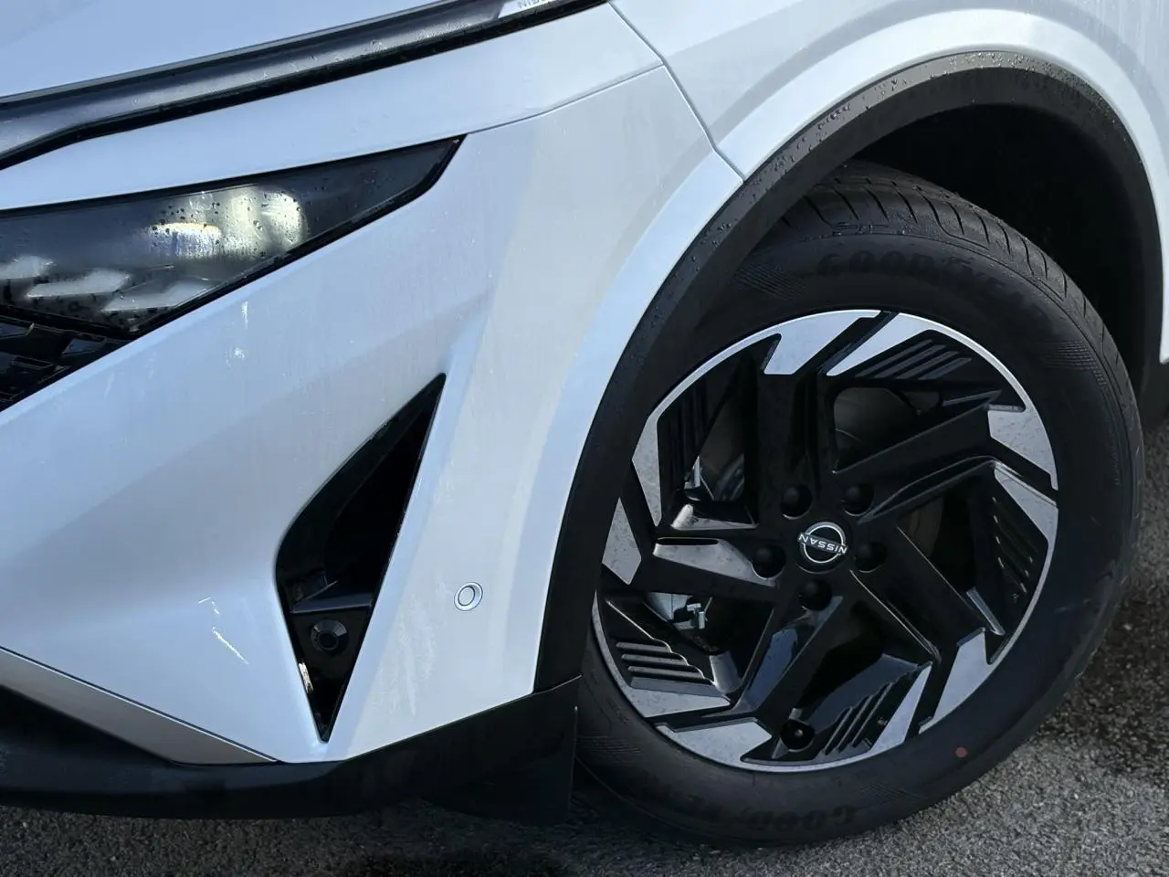 Détail de la roue avant droite et partie avant blanche nacrée du Nissan Qashqai III e-Power avec jante alliage noire et argent.