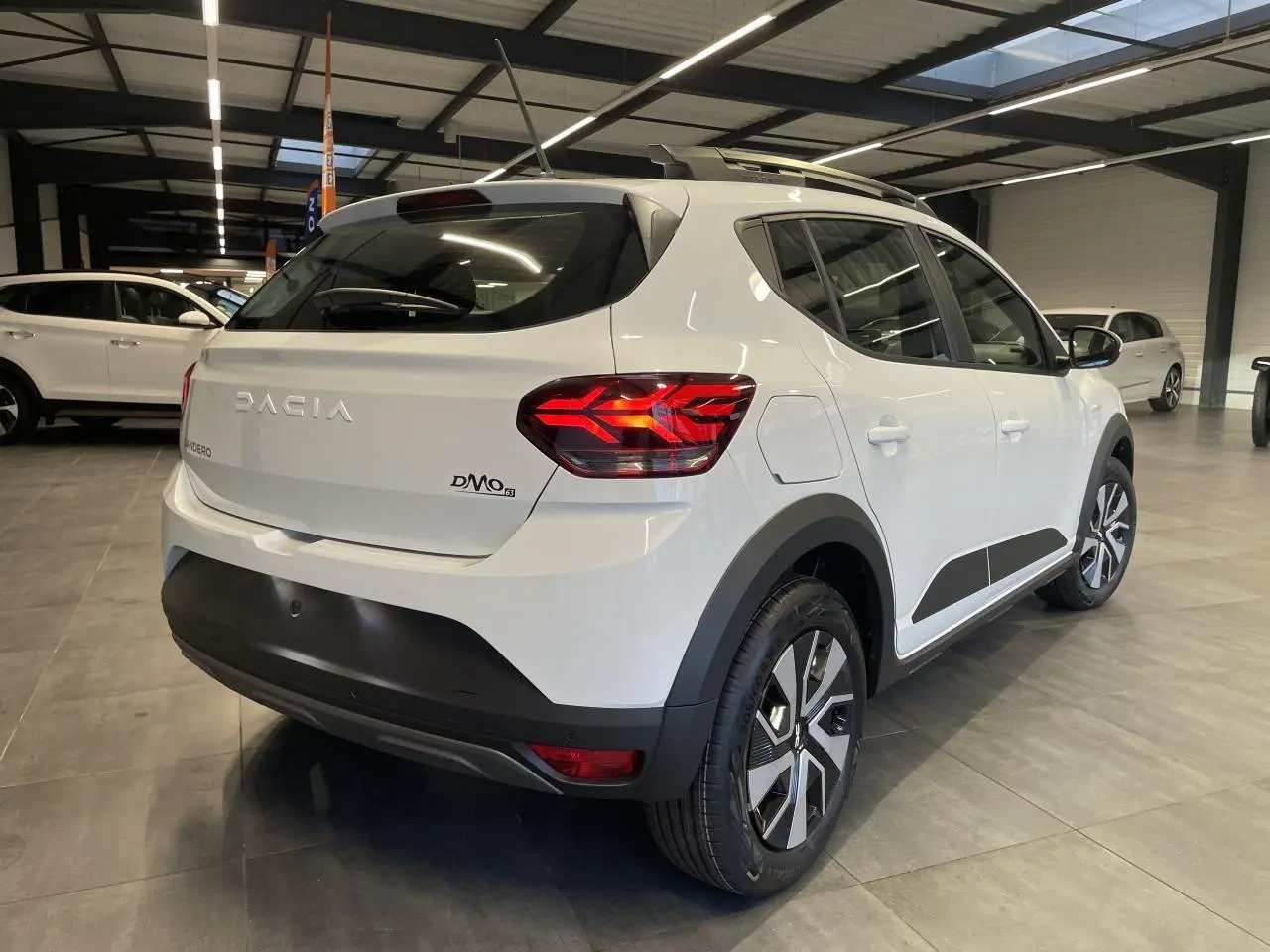 Vue 3/4 arrière droite d'une Dacia Sandero Stepway blanche Glacier avec barres de toit et feux arrière LED en Y.