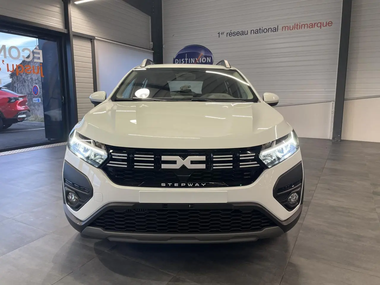 Vue de face du Dacia Sandero Stepway blanc glacier avec calandre noire et signature lumineuse LED allumée.