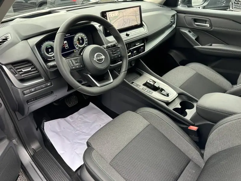 Vue intérieure côté conducteur du Nissan Qashqai Hybrid e-POWER 2025, avec tableau de bord numérique et écran central tactile.
