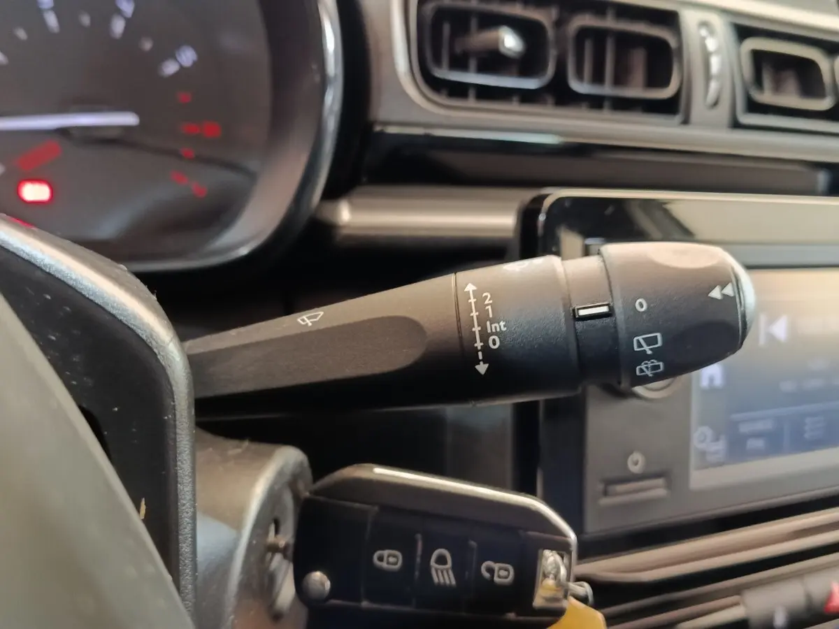 Gros plan sur la commande d’essuie-glace à gauche du volant dans l’habitacle noir de la Citroën C3 blanche.