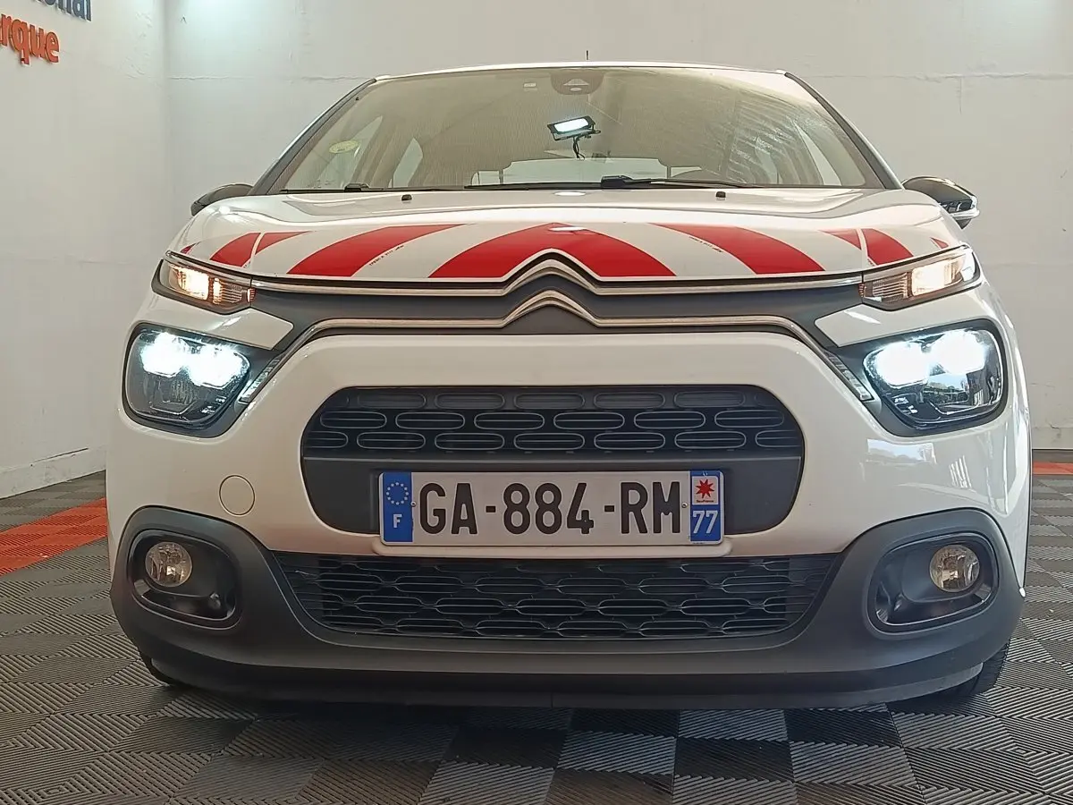 Vue frontale d'une Citroën C3 blanche avec marquage rouge sur le capot et phares allumés en intérieur.