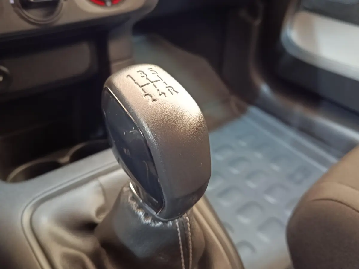 Gros plan sur le levier de vitesses manuel noir de la Citroën C3 blanche, intérieur avec tapis caoutchouc gris.
