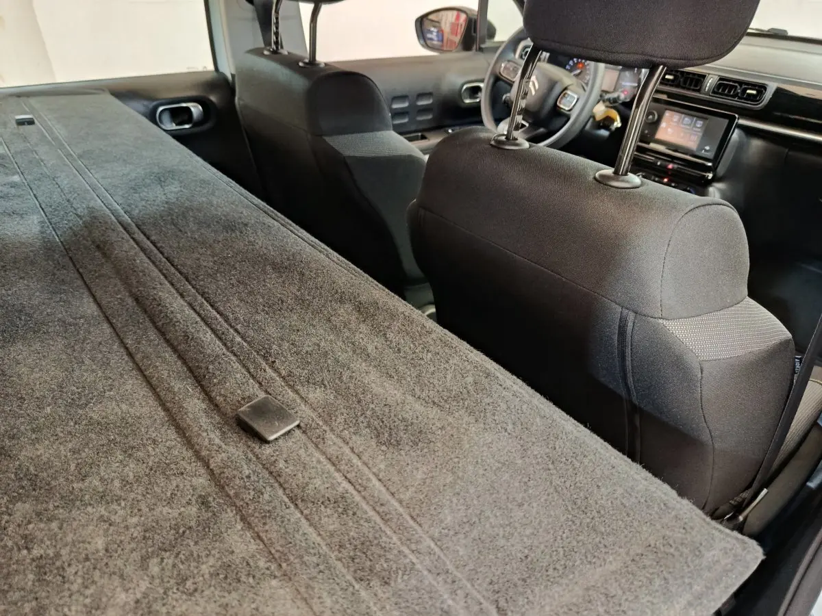 Vue intérieure arrière de la Citroën C3 blanche, banquette rabattue et tableau de bord avec écran tactile visible.