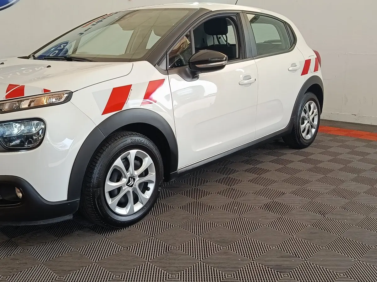 Vue de profil avant droit d'une Citroën C3 blanche 2021 avec marquages rouges sur les ailes et jantes argentées.
