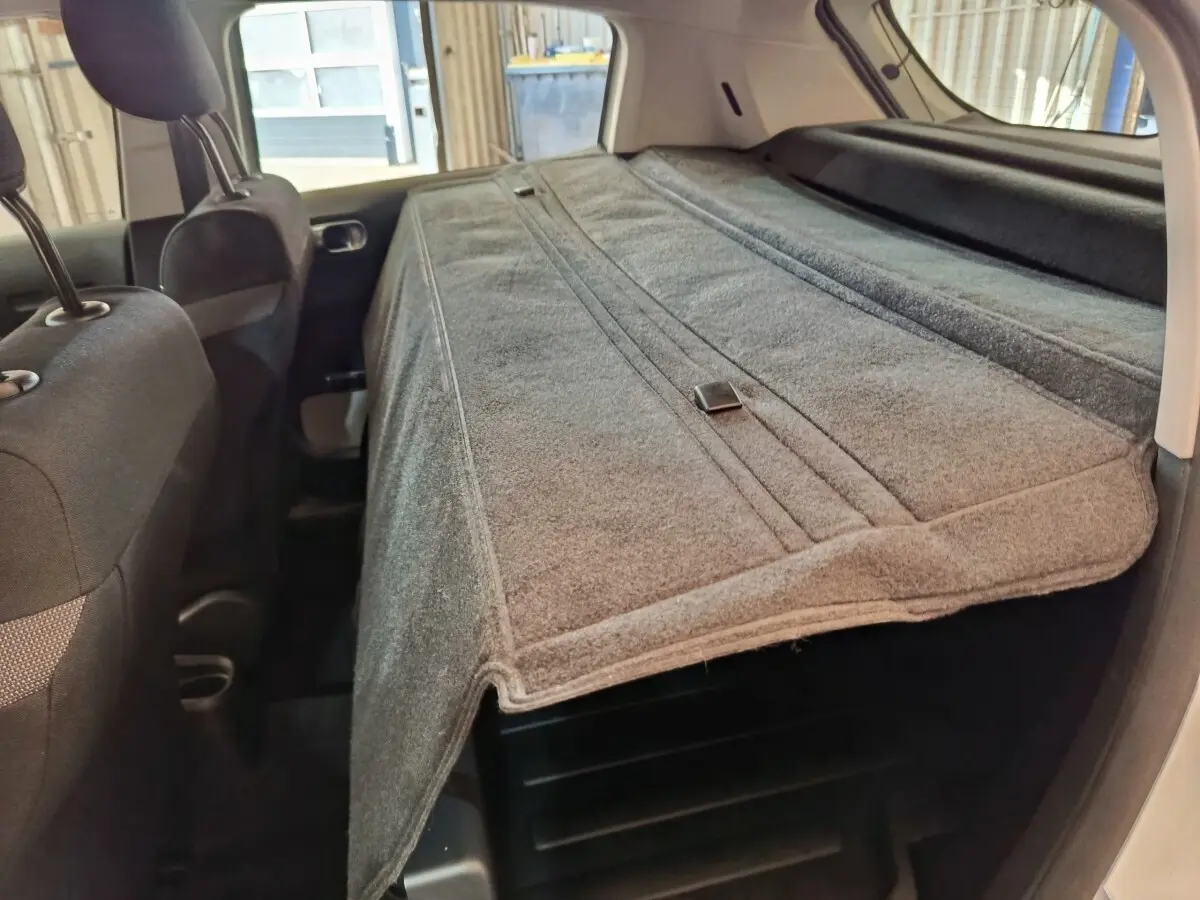 Vue intérieure arrière de la Citroën C3 blanche, mettant en valeur la banquette rabattue et la tablette de coffre grise.