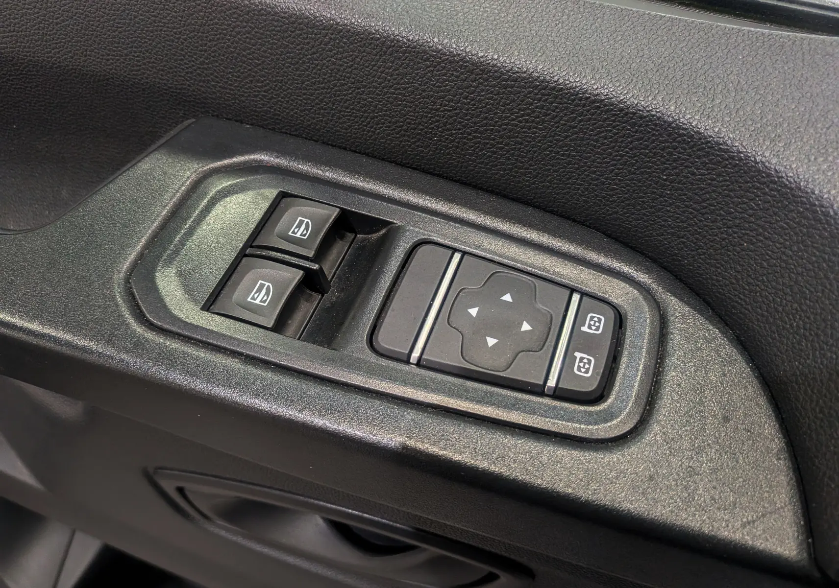 Gros plan sur les commandes de lève-vitres et réglage des rétroviseurs côté conducteur du Renault Trafic Fourgon blanc.
