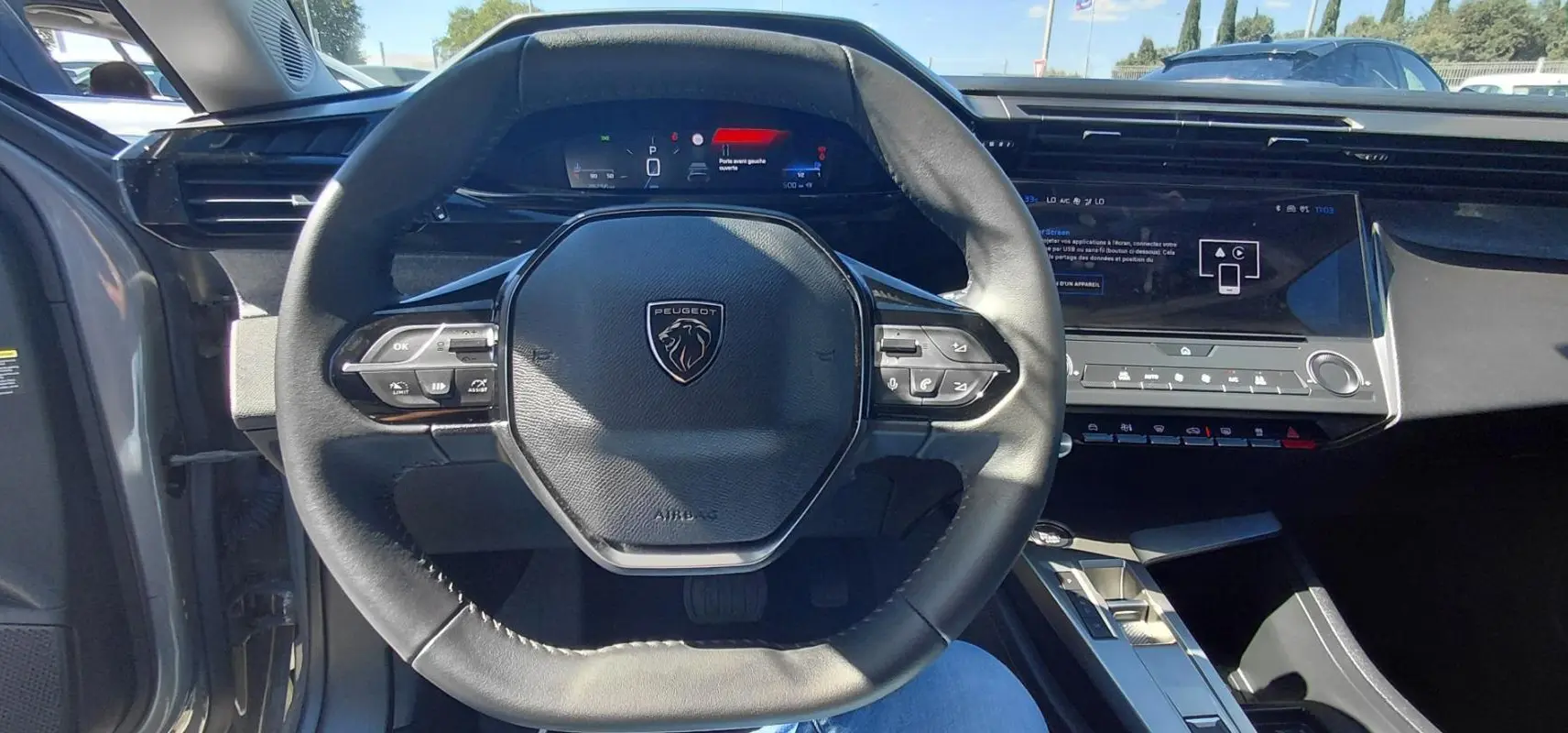 Vue intérieure centrée sur le volant Peugeot 308 gris, avec cockpit numérique et écran tactile de la console centrale.