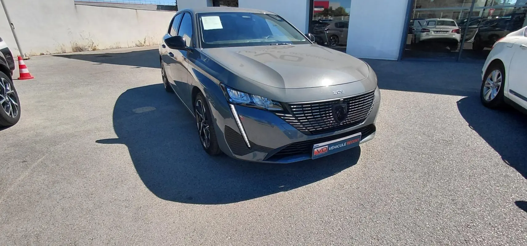PEUGEOT 308 gris en 3/4 avant droit, avec calandre noire distinctive et jantes alliage 17 pouces visibles.