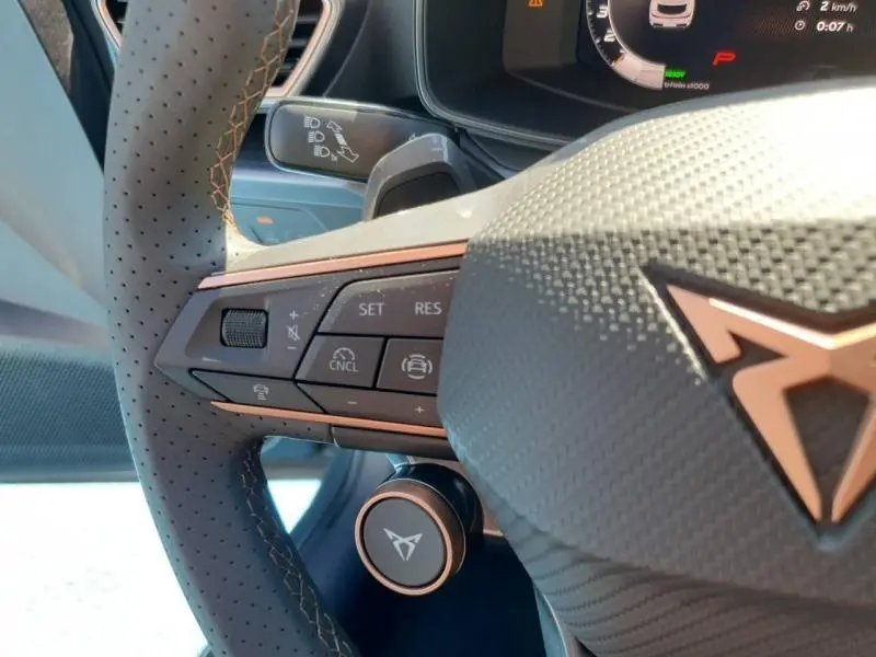 Gros plan sur le volant cuir perforé gris du CUPRA Formentor bleu, avec commandes multifonctions et logo CUPRA rosé.