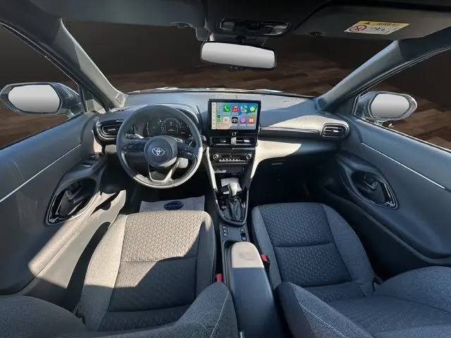 Vue intérieure avant de la Toyota Yaris Cross 130H Design 2025, tableau de bord avec écran tactile et sièges tissu gris.