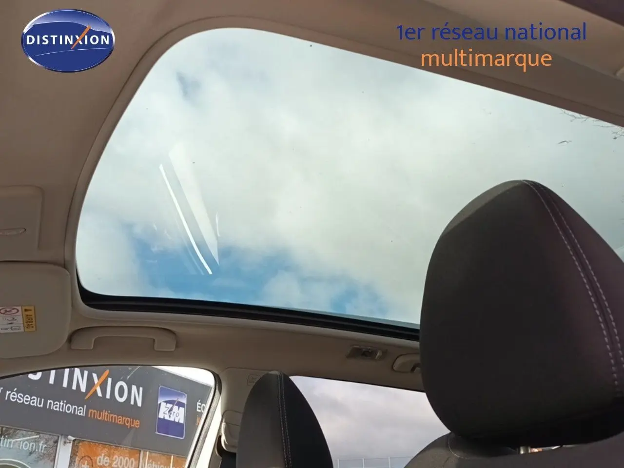 Vue intérieure du toit ouvrant panoramique du Nissan Qashqai blanc, avec appuie-tête avant en tissu noir visible.