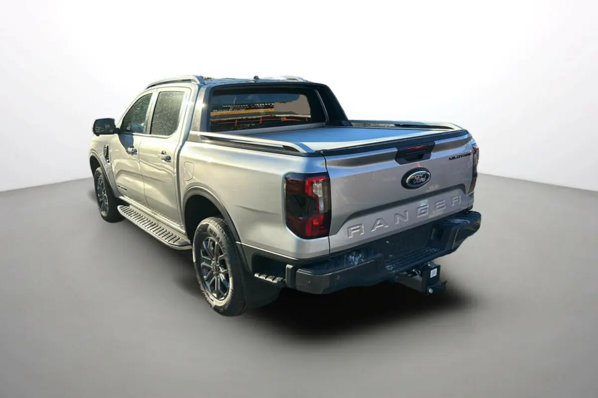 Ford Ranger 2.0 205 Wildtrak Plus gris iconic, vue 3/4 arrière droit avec attelage et bac de benne fermé.