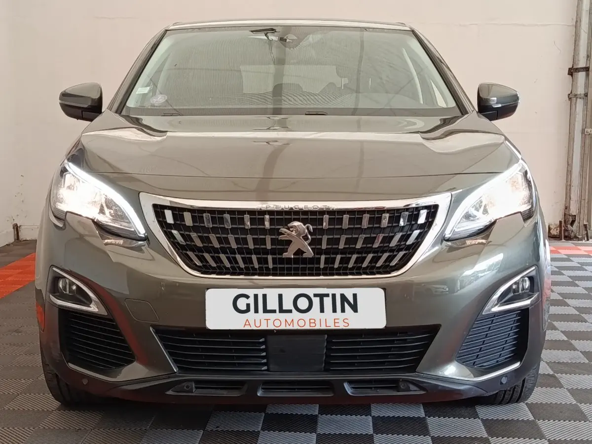 Vue frontale d'un Peugeot 5008 gris foncé avec calandre chromée et feux LED allumés dans un garage.
