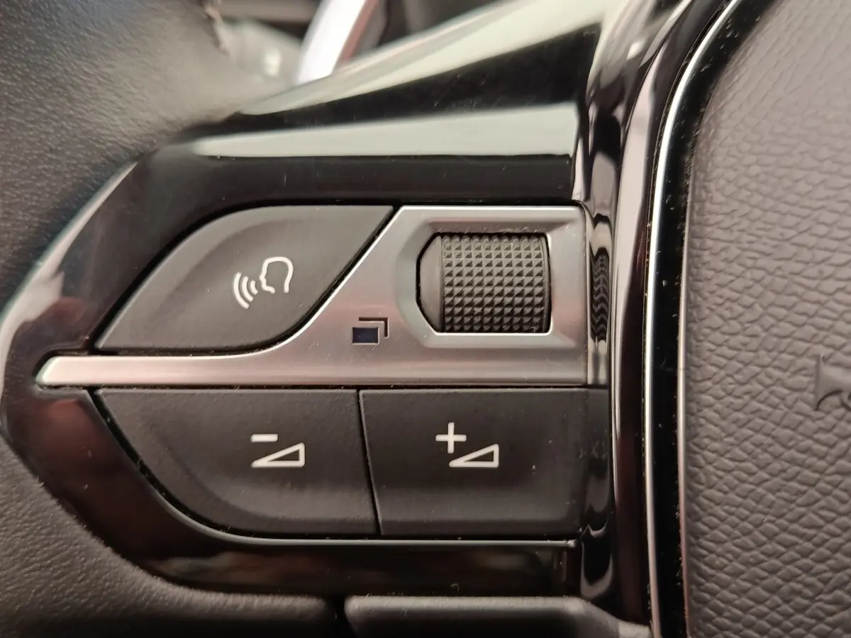 Gros plan sur les commandes vocales et volume au volant cuir noir du Peugeot 5008 gris foncé, version 2020.