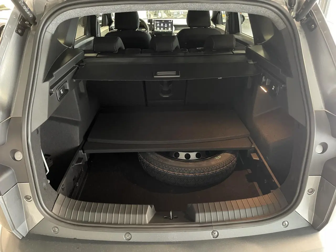 Vue arrière du coffre ouvert du Dacia Bigster gris schiste, montrant la roue de secours et la tablette de rangement.