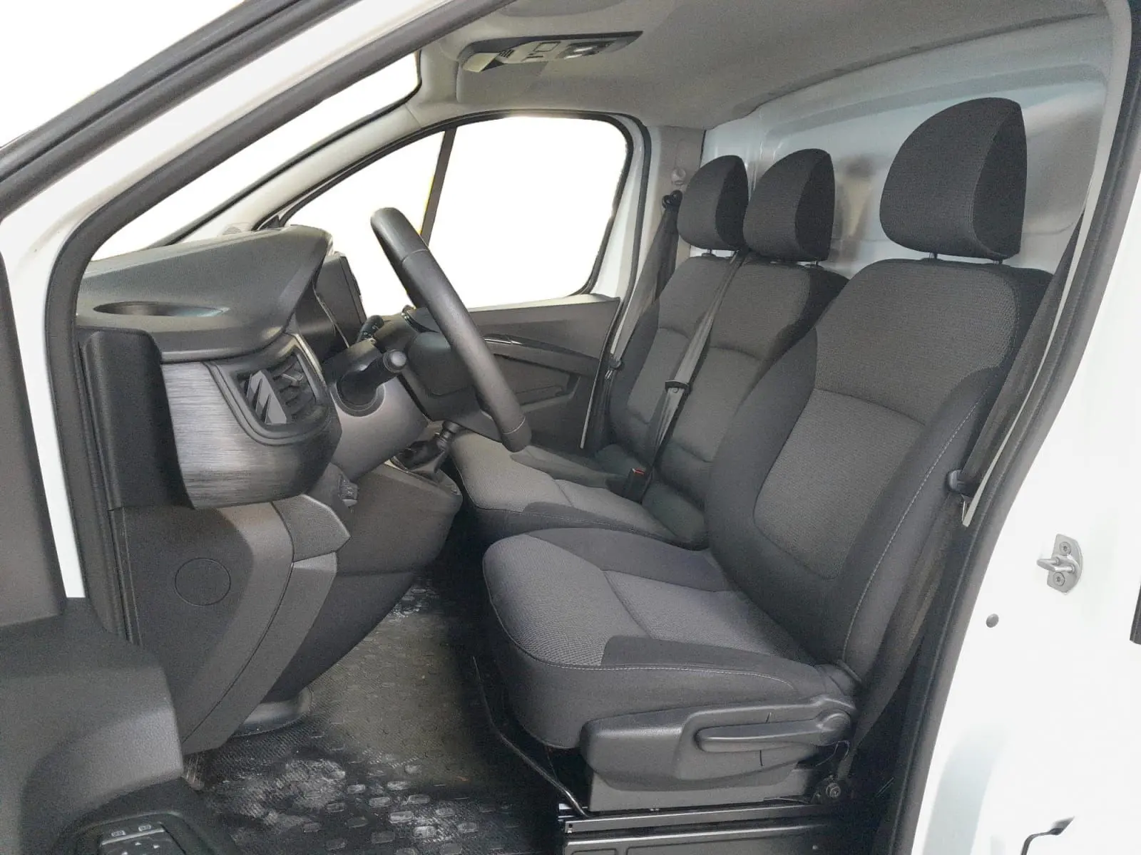 Vue intérieure côté conducteur du Renault Trafic Fourgon blanc, montrant les sièges tissu gris et le tableau de bord minimaliste.