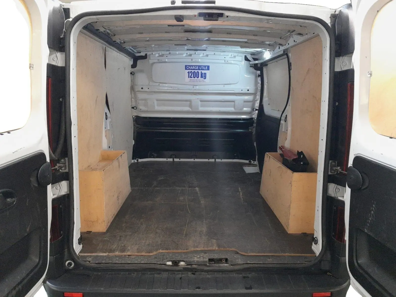 Vue arrière ouverte du Renault Trafic Fourgon blanc minéral 2024, montrant l’espace de chargement avec panneaux en bois et capacité 1200 kg.