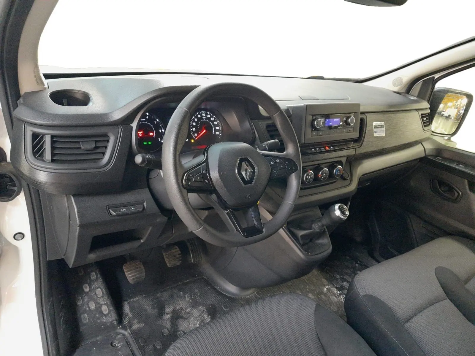 Vue intérieure côté conducteur du Renault Trafic Fourgon 2024, tableau de bord noir avec volant multifonction et levier de vitesse manuel.