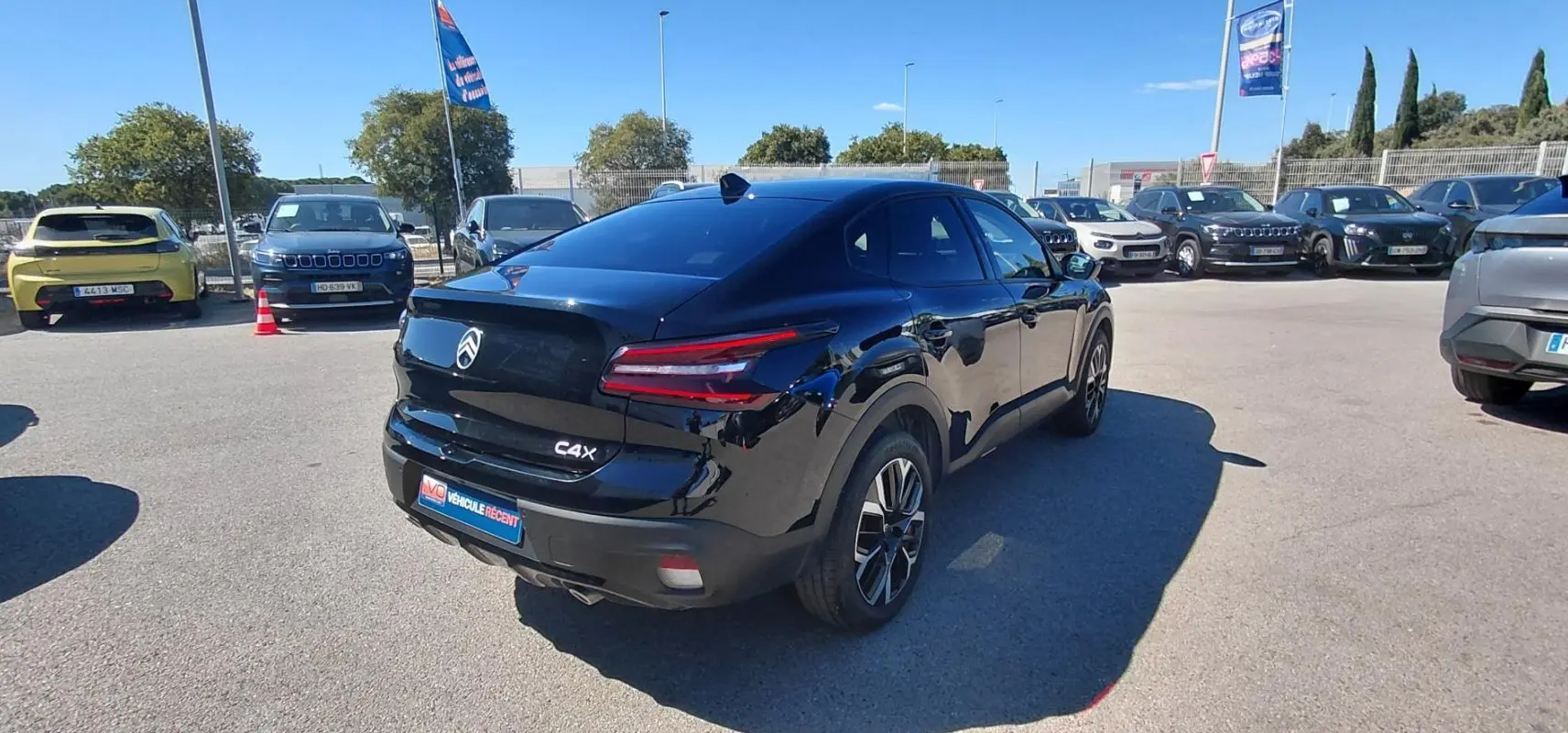 Vue 3/4 arrière droite d'une Citroën C4 X noire avec jantes alliage 17 pouces sur parking ensoleillé.