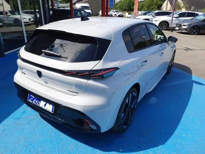 Vue 3/4 arrière droite d’une Peugeot 308 blanche Okénite avec vitres arrière surteintées et jantes alu noires.
