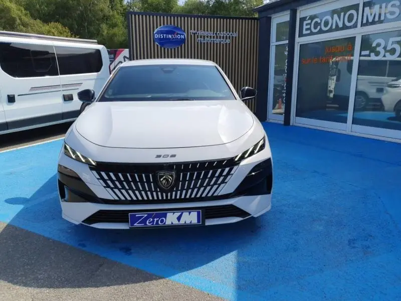 Vue frontale d'une Peugeot 308 blanche Okénite avec calandre distinctive et phares LED fins.