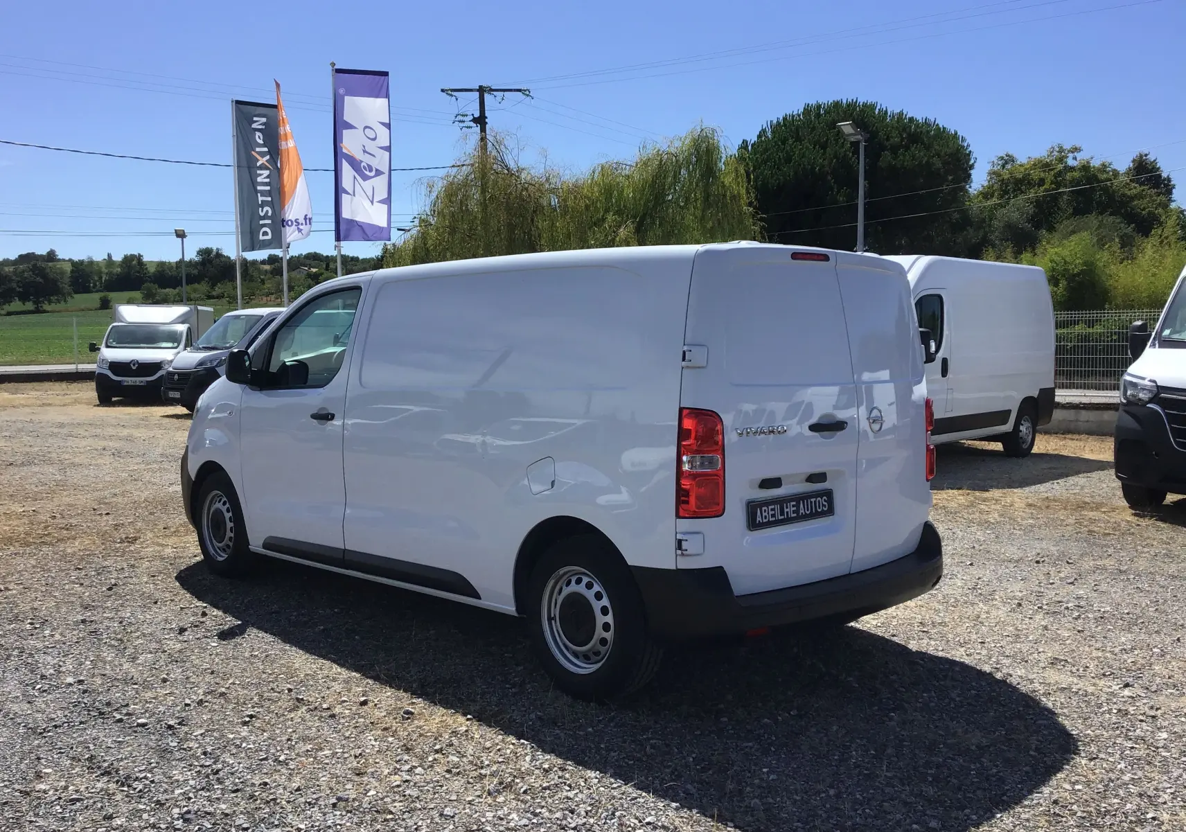Vue 3/4 arrière droite d'un utilitaire Opel Vivaro blanc 2023 stationné sur un terrain extérieur.