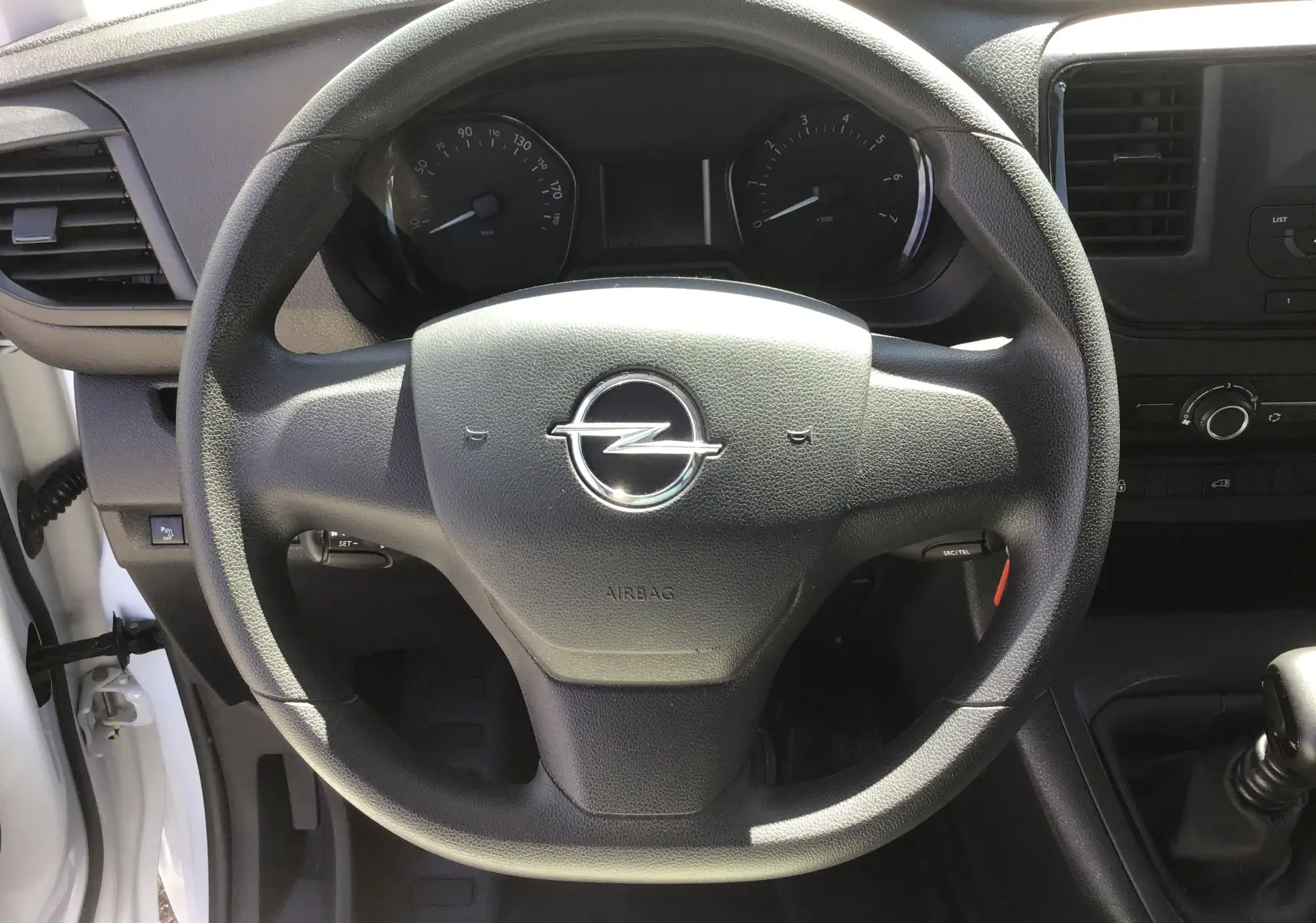 Vue rapprochée du volant noir de l'Opel Vivaro blanc 2023, avec tableau de bord et levier de vitesse manuel visibles.