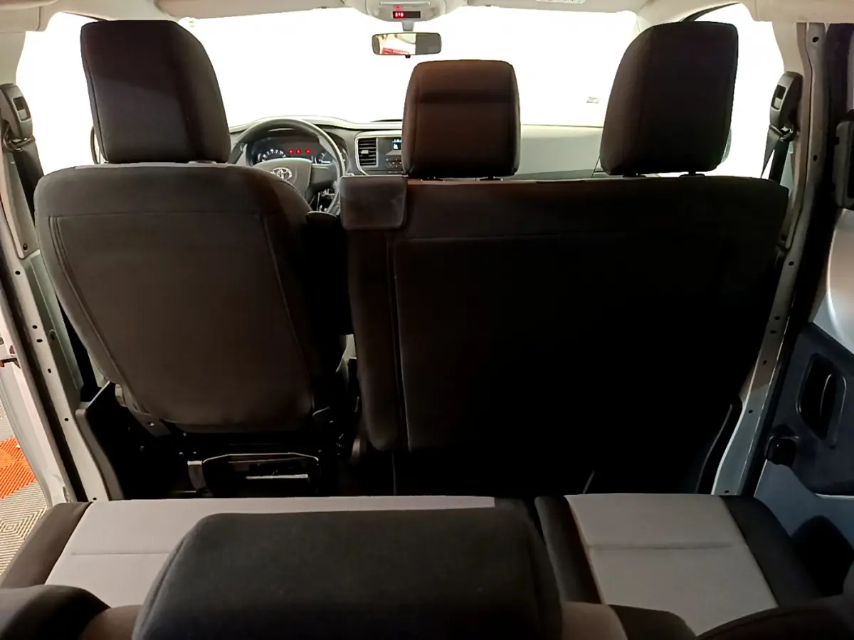 Vue arrière intérieure du Toyota Proace Verso 2019, sièges noirs et gris, tableau de bord et volant visibles au loin.