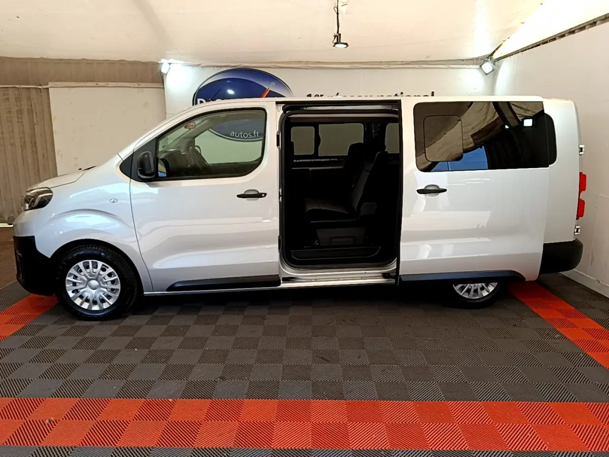 Profil latéral droit d'un Toyota Proace Verso gris clair avec porte coulissante ouverte dévoilant l'intérieur sombre.