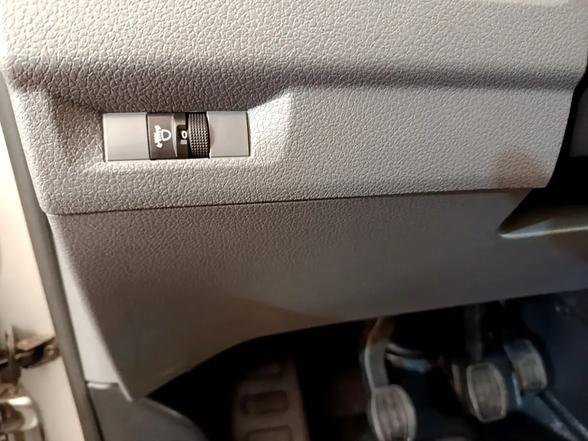 Détail du tableau de bord gris clair du Toyota Proace Verso 2019 montrant le réglage manuel des phares et les pédales côté conducteur.