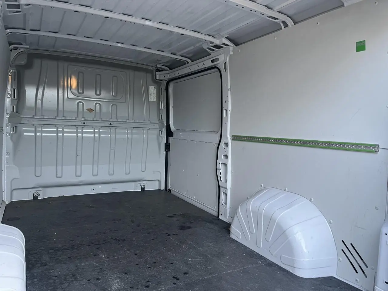 Vue intérieure arrière du fourgon Opel Movano blanc, montrant l'espace de chargement avec plancher et parois métalliques.