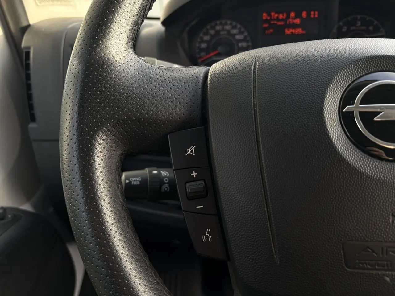 Gros plan sur le volant noir perforé d’un Opel Movano Fourgon 2024 avec commandes intégrées et logo Opel visible.