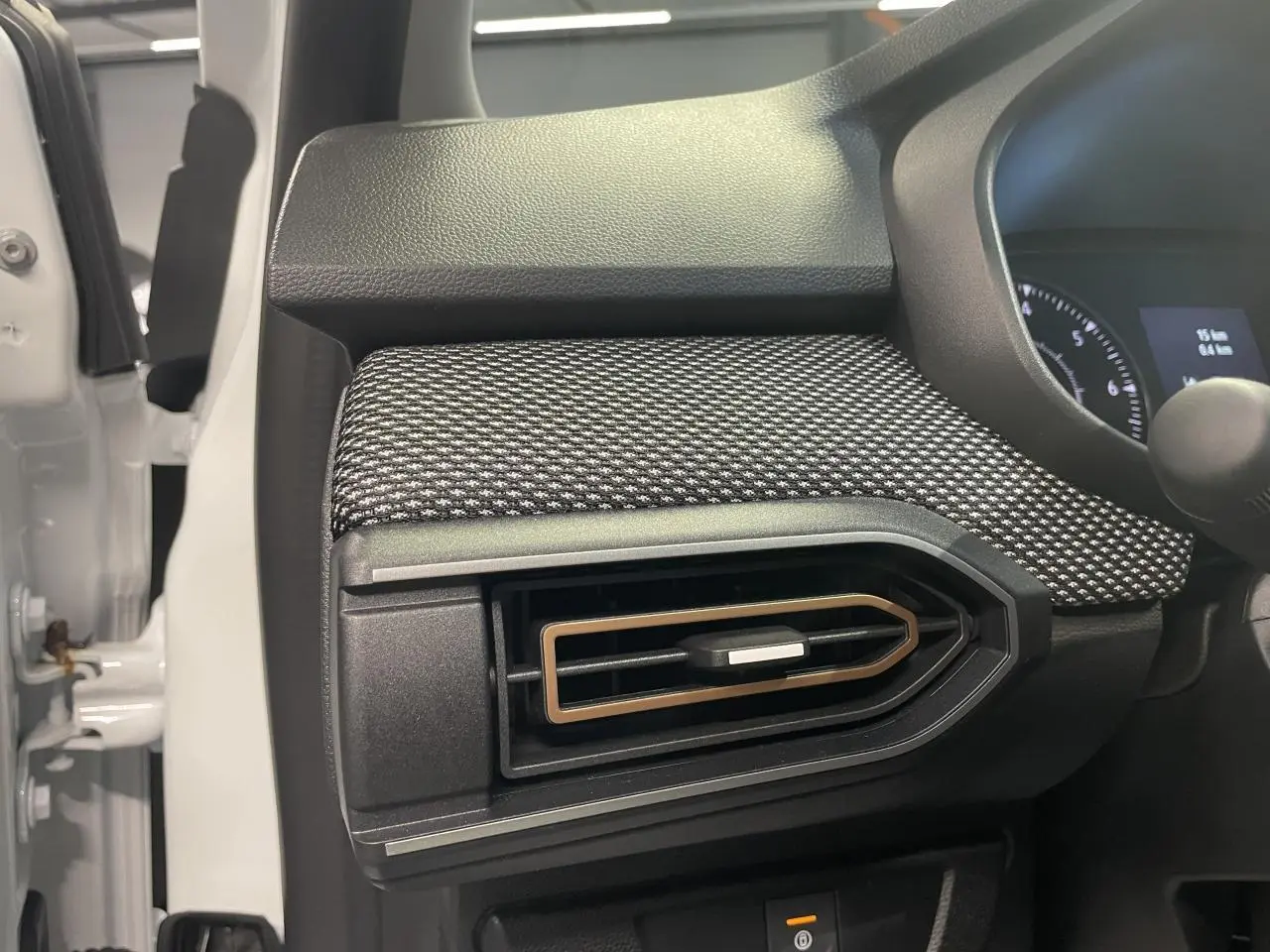 Détail de l'aérateur latéral droit avec insert brun cuivré sur tableau de bord noir et tissu gris de la Dacia Sandero blanche.