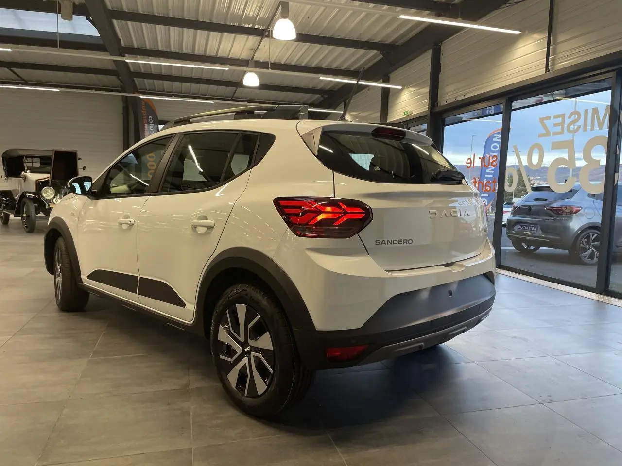 Vue 3/4 arrière droite d'une Dacia Sandero Stepway blanche Glacier avec barres de toit et jantes spécifiques en concession.