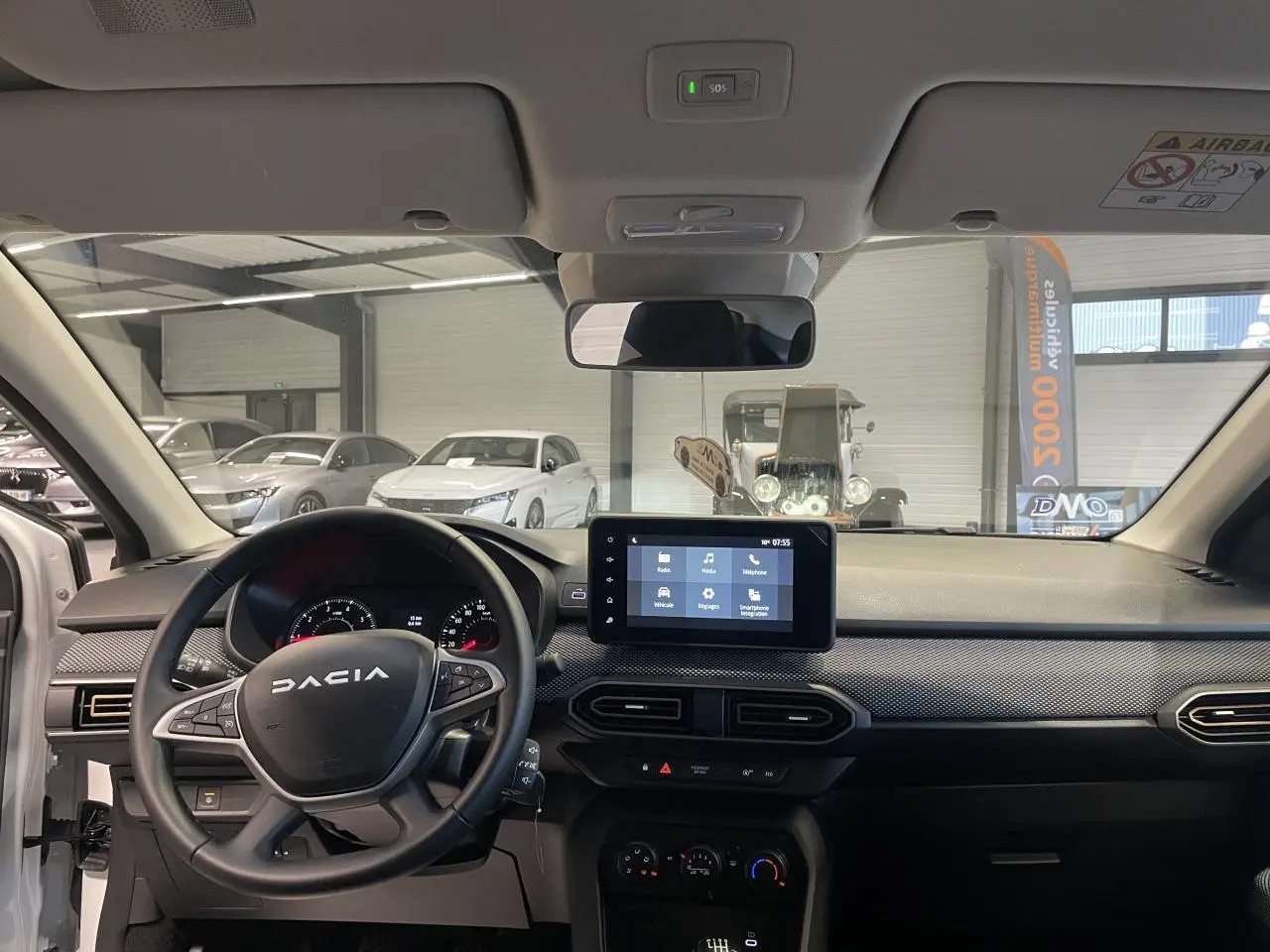 Vue intérieure avant du tableau de bord de la Dacia Sandero blanc glacier avec écran tactile et volant multifonction.