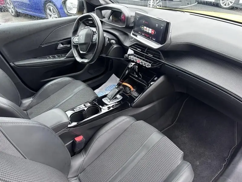 Vue intérieure côté conducteur de la Peugeot 208 jaune 2021, mettant en valeur le tableau de bord et la console centrale moderne.