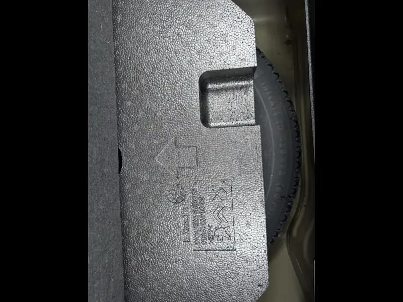 Détail du coffre d’une Peugeot 208 jaune 2021, montrant la roue de secours partiellement recouverte par un panneau en mousse grise.