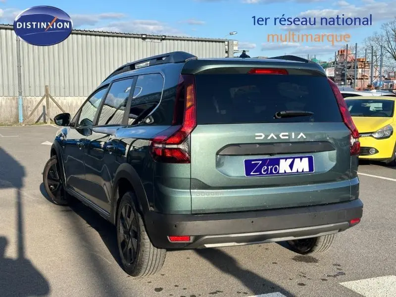 Vue 3/4 arrière droite d'un Dacia Jogger 2025 vert cèdre métallisé avec barres de toit et feux arrière LED.