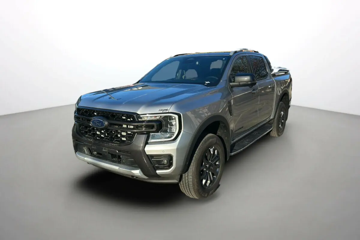 Ford Ranger 2.0 205 Wildtrak Plus gris iconic en 3/4 avant avec jantes alu noires et barres de toit visibles.
