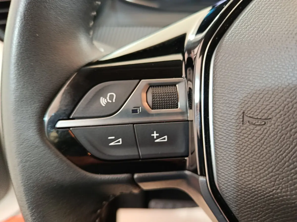 Gros plan sur les commandes gauche du volant cuir multifonctions de la Peugeot 208 électrique blanche, année 2022.