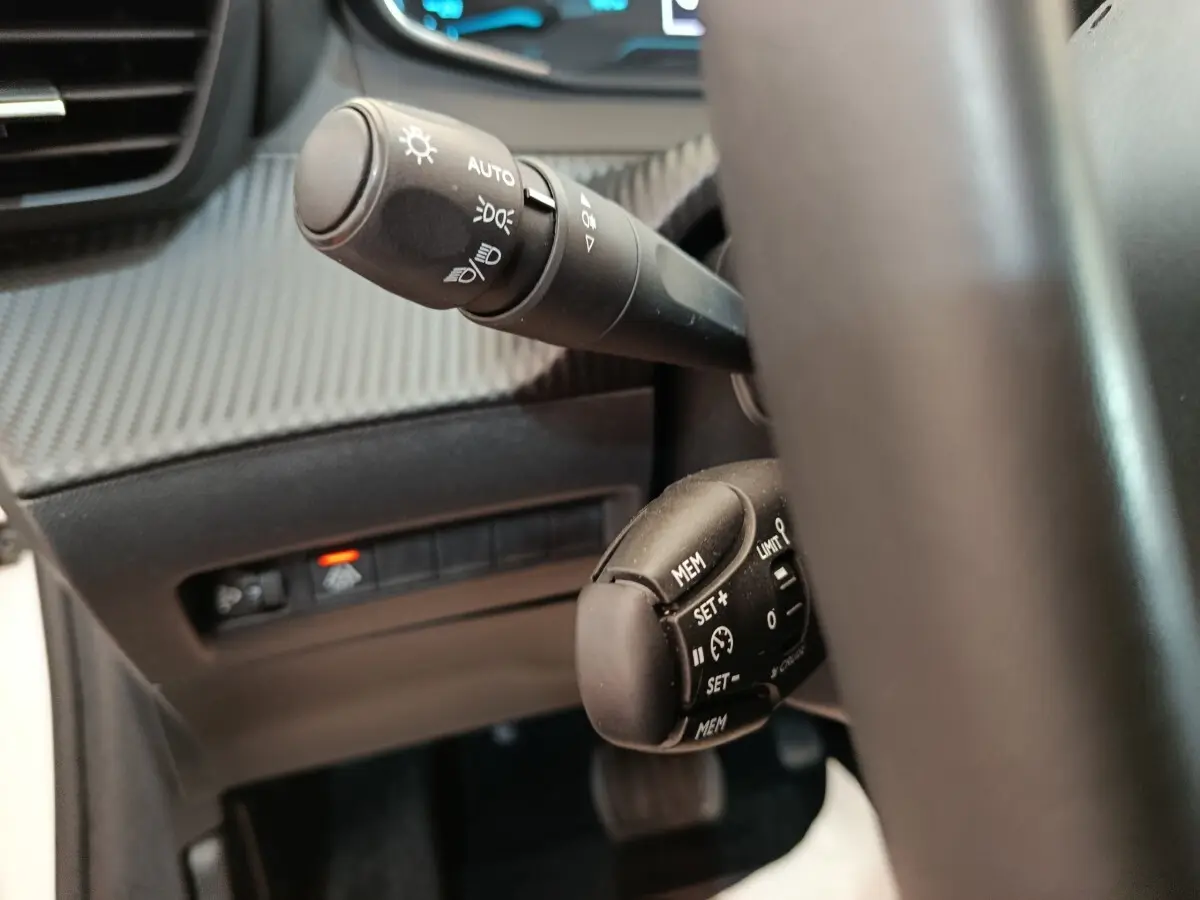 Gros plan sur les commandes au volant noir de la Peugeot 208 électrique Active Business R, tableau de bord en arrière-plan.