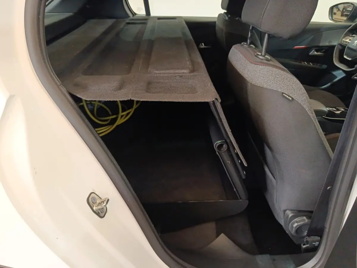 Vue intérieure côté arrière droit d'une Peugeot 208 électrique blanche avec banquette rabattue et coffre ouvert.
