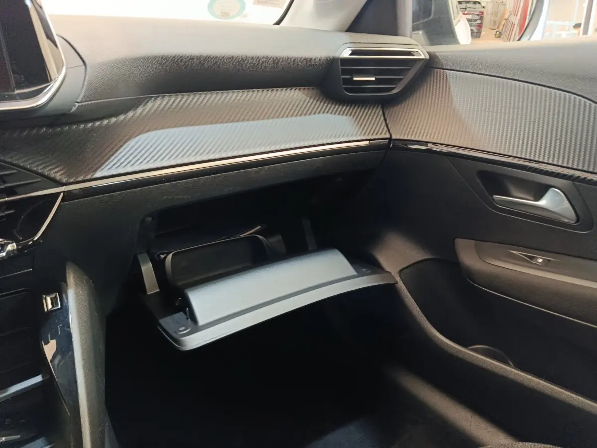 Intérieur côté passager de la Peugeot 208 électrique 2022, tableau de bord noir avec boîte à gants ouverte.