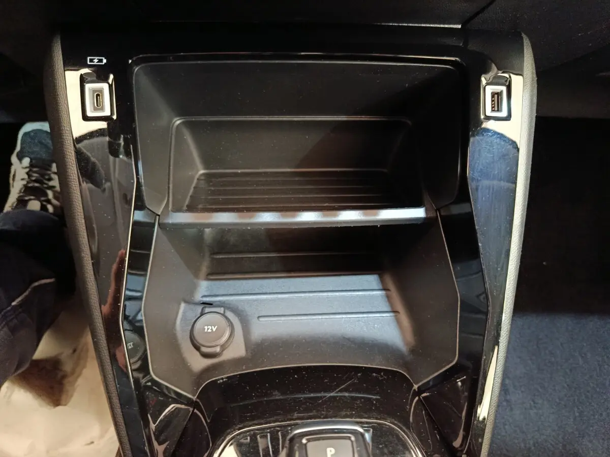 Vue rapprochée de la console centrale noire du Peugeot 208 électrique 2022 avec prise 12V et ports USB visibles.