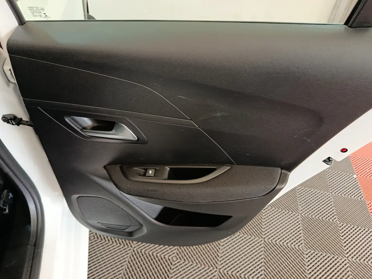 Vue intérieure côté gauche de la porte avant noire d'une Peugeot 208 électrique blanche, avec poignée et commande de vitre.