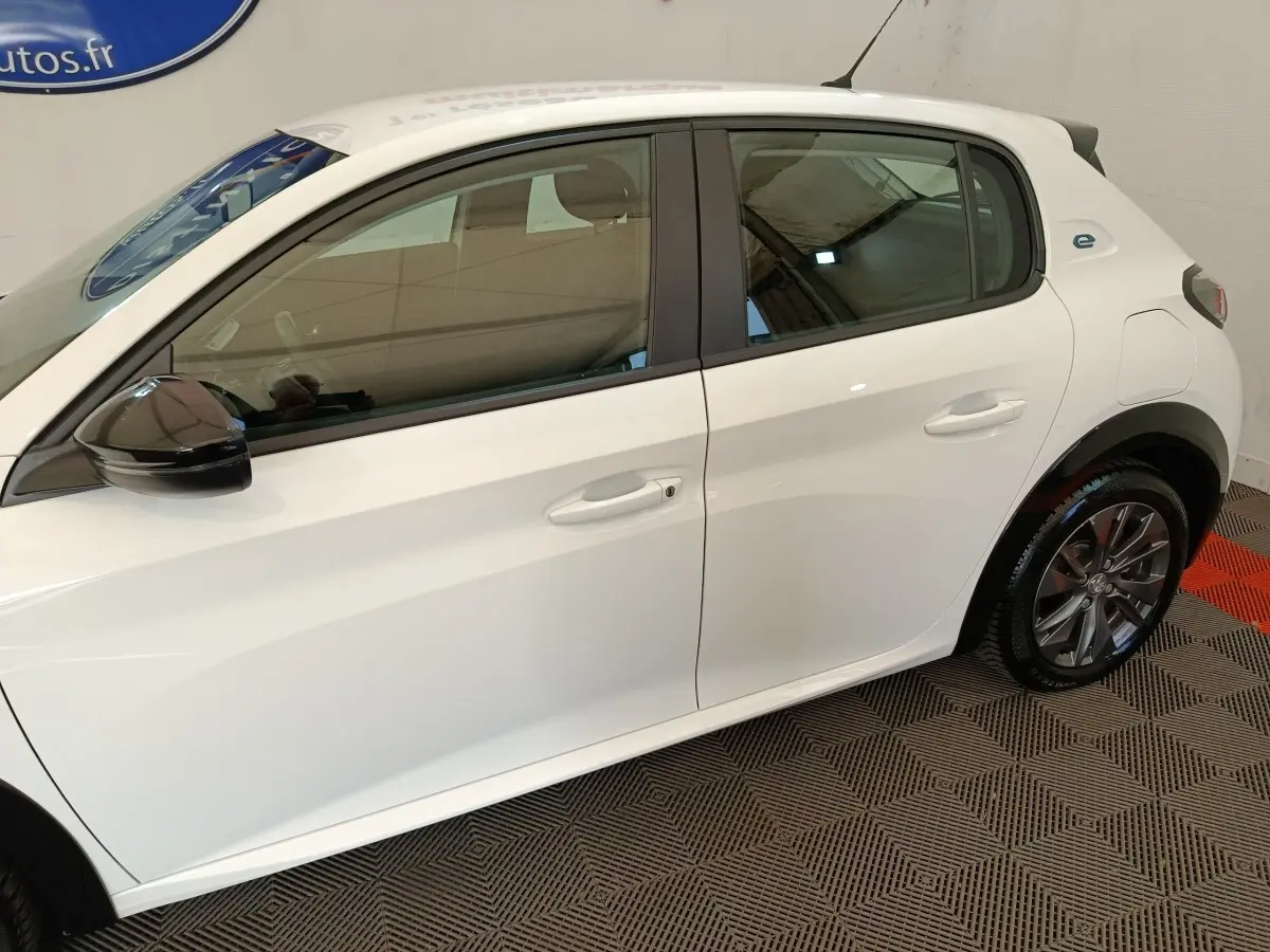 Vue latérale droite d'une Peugeot 208 électrique blanche avec rétroviseur noir et jantes alliage gris.