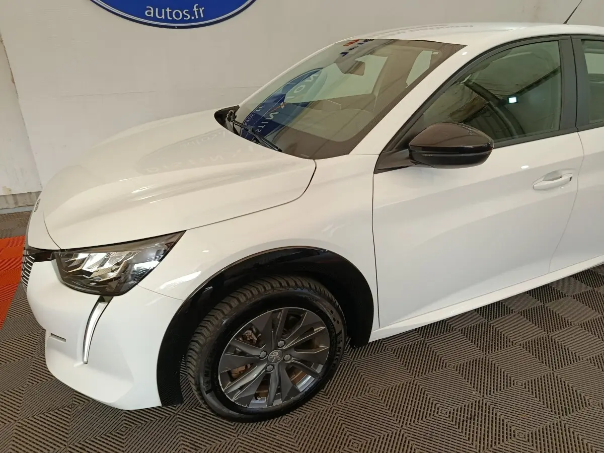 Peugeot 208 électrique blanche vue 3/4 avant droit avec jantes foncées et rétroviseur noir brillant.